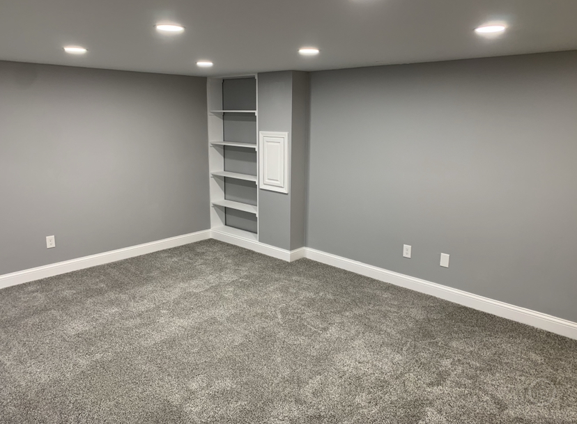 A finished basement with recessed lighting, built-in shelving, and new carpet